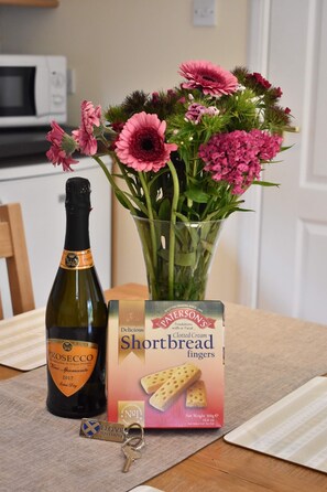 A bottle of Prosecco, a box of clotted cream fingers, a keychain, and a vase with pink flowers on a table.