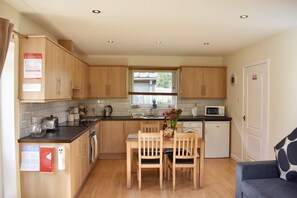 A compact kitchen with wooden cabinets, a dining table with chairs, a microwave, and a small dishwasher.