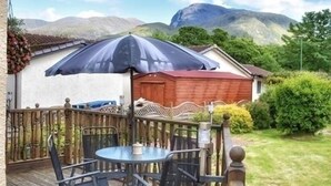 Eine Holzterrasse mit rundem Tisch, Stühlen, einem großen Sonnenschirm und einem Blumentopf.