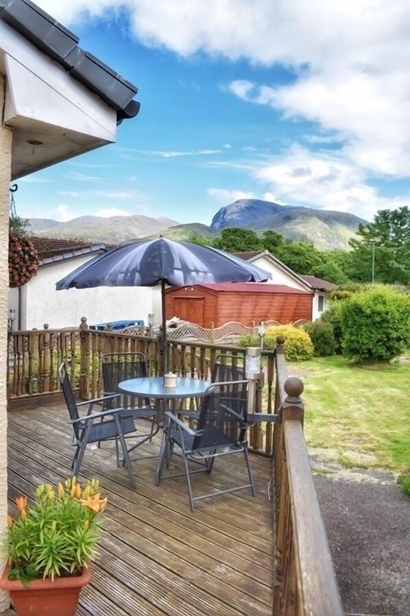 A wooden deck with a round table and chairs, a large umbrella, and a potted plant.