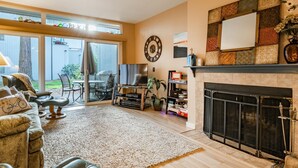 A spacious living room with a fireplace, a television, and a dining area with outdoor access. - JL 615: Quiet close to pool and beach, free Wi-Fi! (Birch Bay)