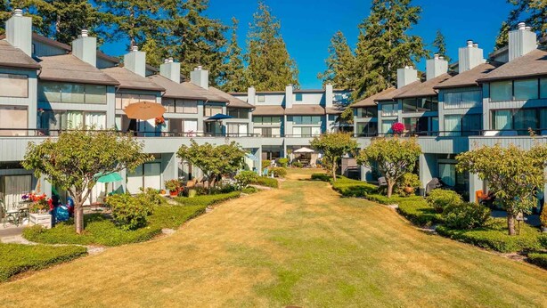 A row of modern multi-story buildings with a central courtyard, surrounded by trees and greenery. - JL 615: Quiet close to pool and beach, free Wi-Fi! (Birch Bay)