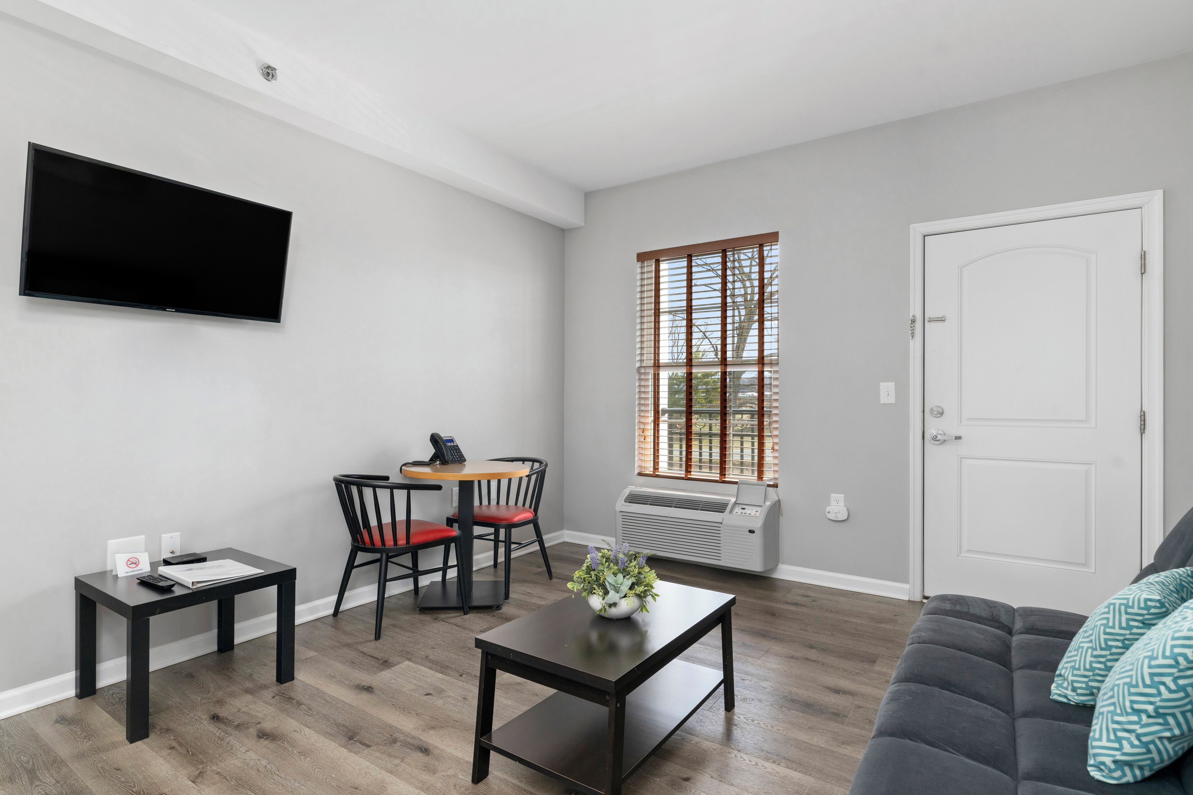 Una sala de estar moderna con un televisor de pantalla plana, un comedor con mesa y sillas, un sofá y un ventanal con persianas.