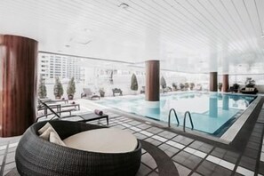Ein moderner, überdachter Poolbereich mit großen Glaswänden, einem Pool und Liegemöglichkeiten.