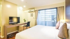 A hotel room with a bed, a desk with a television, a chair, and a window with curtains. - Parkroyal Suites Bangkok (Bangkok)