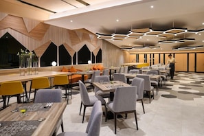 A modern dining area with multiple tables and chairs, geometric ceiling design, and a person serving.