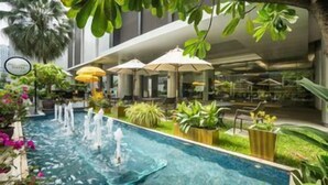 A swimming pool with fountains, surrounded by greenery and outdoor seating areas. - Parkroyal Suites Bangkok (Bangkok)