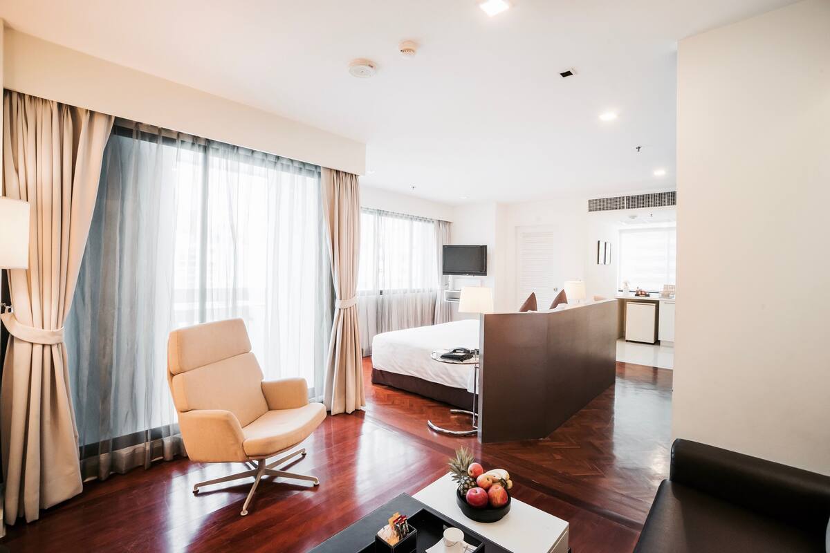 Ein Hotelzimmer mit Bett, Schreibtisch, Stuhl, einem Couchtisch mit Früchten und einem Fernseher.