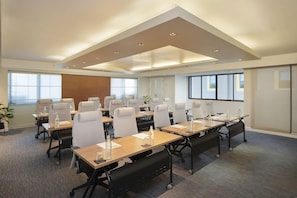 A conference room with multiple tables and chairs, large windows, and a modern ceiling design.