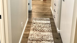 A hallway with a patterned rug, white walls, and a kitchen area in the background. - Beautifully remodeled, clean, well-stocked entire home - sleeps 7! (Yakima)
