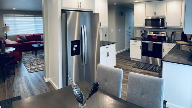 A modern kitchen with stainless steel appliances, white cabinetry, and a dining area with a table and chairs. - Beautifully remodeled, clean, well-stocked entire home - sleeps 7! (Yakima)