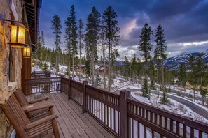 A wooden deck with a railing overlooking a snowy landscape with trees and mountains. - Grace Manor (Breckenridge)
