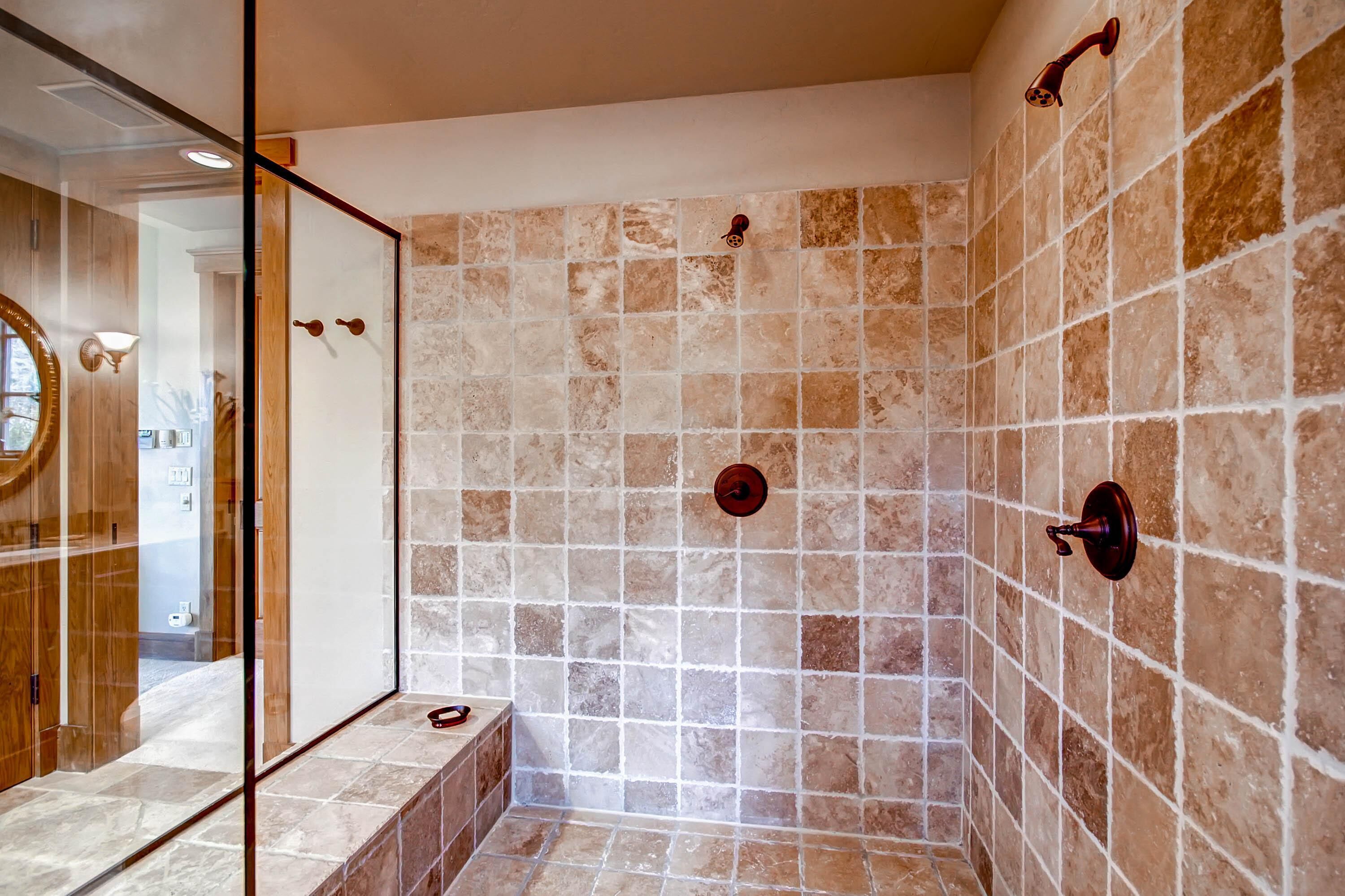 A shower with beige tiles and a wooden bench.