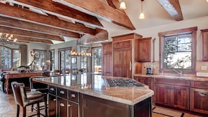 A spacious kitchen with a large island, wooden cabinets, and a high ceiling with exposed beams. - Rustic Timber Lodge (Breckenridge)