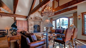 A spacious living room with a stone fireplace, leather furniture, and a large window offering a mountain view. - Rustic Timber Lodge (Breckenridge)