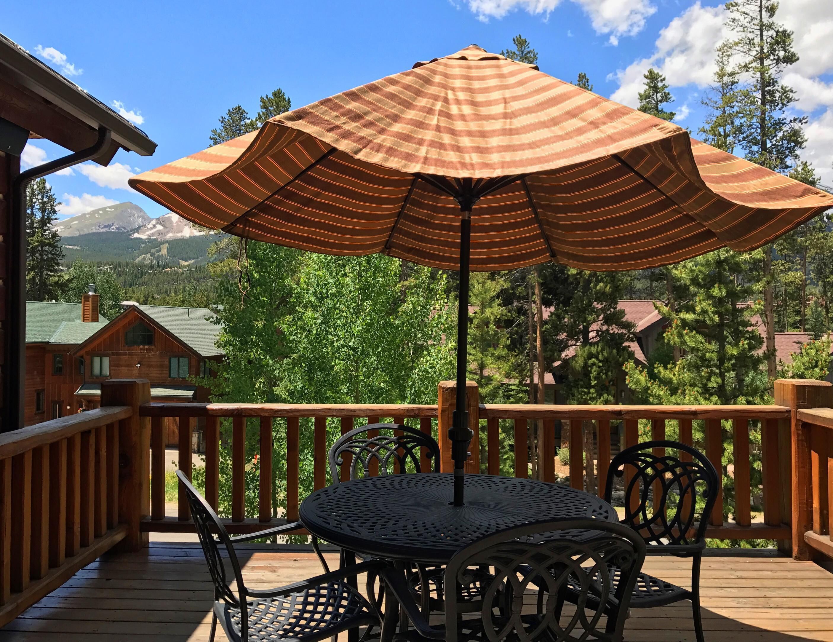 A wooden deck with a round table and chairs, an umbrella, and a mountain view.