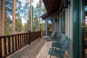 A wooden deck with a railing, surrounded by tall trees, and featuring outdoor seating. - Beaver's Lodge (Breckenridge)