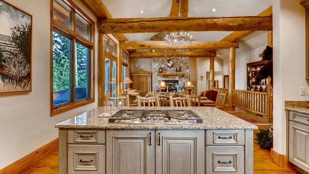 A spacious kitchen with a large island, wooden beams, and a stone fireplace. - Beaver's Lodge (Breckenridge)