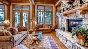 A cozy living room with a stone fireplace, large windows, and a comfortable seating area. - Beaver's Lodge (Breckenridge)