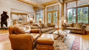 A spacious living room with leather furniture, large windows, and a view of the forest. - Beaver's Lodge (Breckenridge)