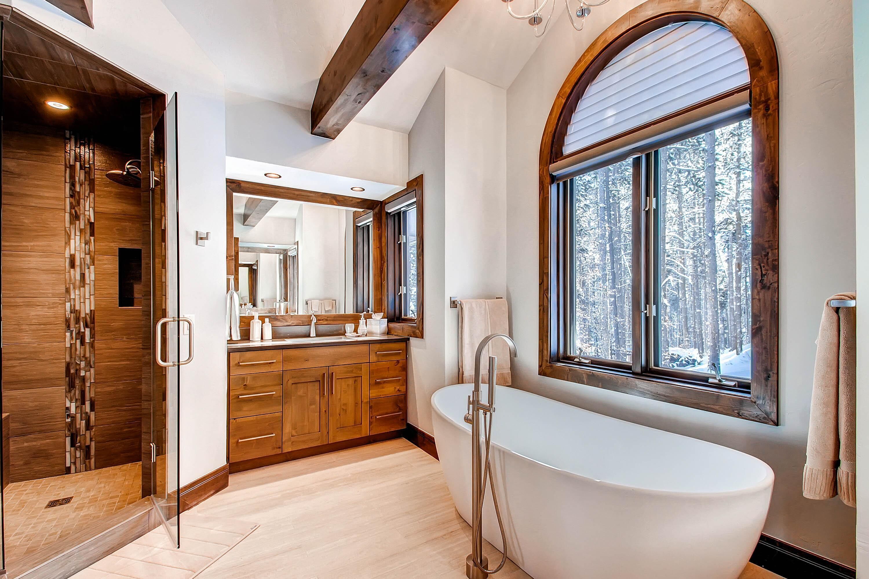 Une salle de bain moderne avec une baignoire sur pieds, des meubles en bois, un grand miroir et une fenêtre donnant sur un paysage enneigé.