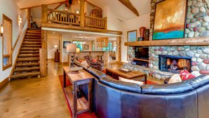 A spacious living area with a stone fireplace, a wooden staircase, and a comfortable seating area. - Inglenook (Breckenridge)