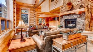 L’intérieur d’une cabane en rondins, avec une cheminée en pierre, des meubles en bois et un coin salon confortable.