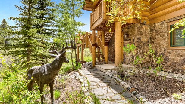 Une cabane en bois avec une façade en pierre, un chemin en pierre et une statue de cerf.