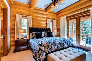 A log cabin bedroom with a large bed, wooden headboard, and a balcony with outdoor seating.