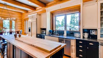 A modern kitchen with wooden beams, a large island, and a window overlooking a forest.