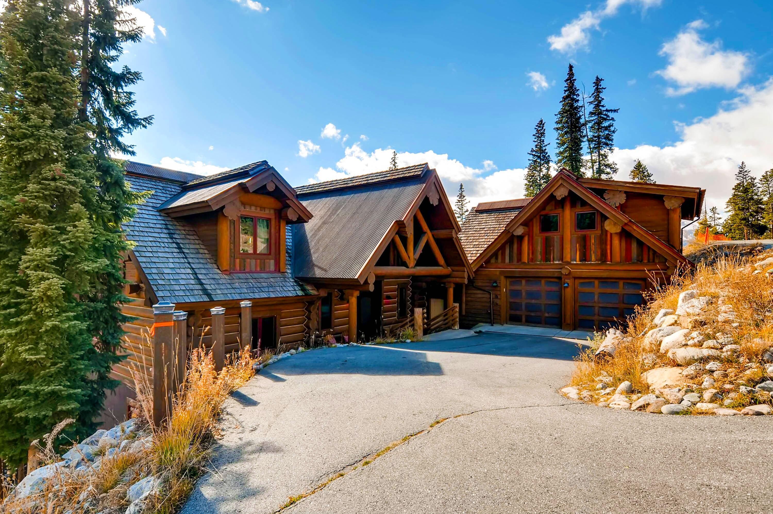 A log cabin with a garage, surrounded by trees and a clear sky.