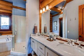A bathroom with a glass-enclosed shower, a large vanity with two sinks, and a large mirror.