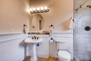 Une salle de bain comprenant un lavabo sur colonne, des toilettes, une douche avec des portes en verre et un meuble-lavabo avec un miroir et un porte-serviettes.
