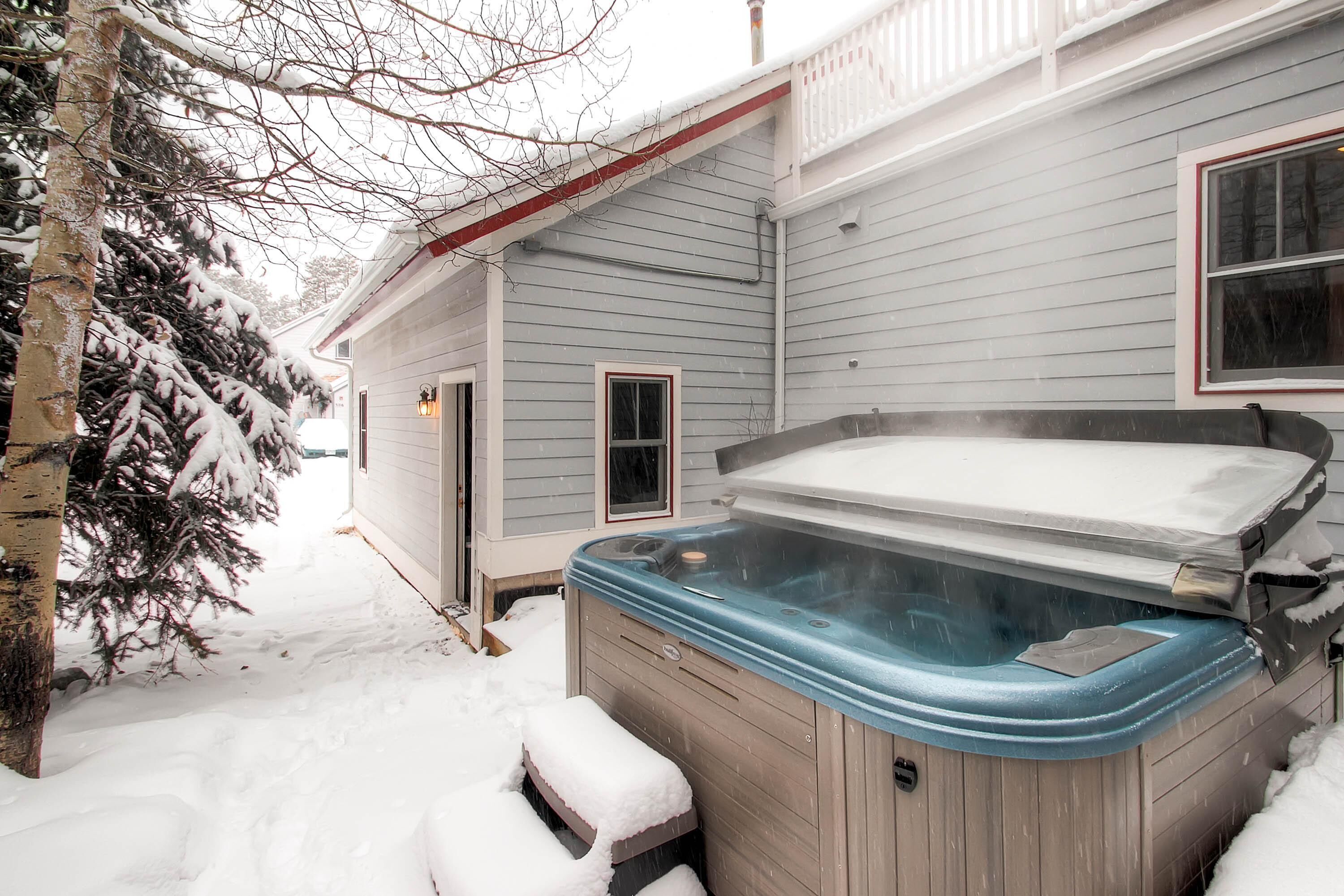A house with a hot tub in the backyard, surrounded by snow.