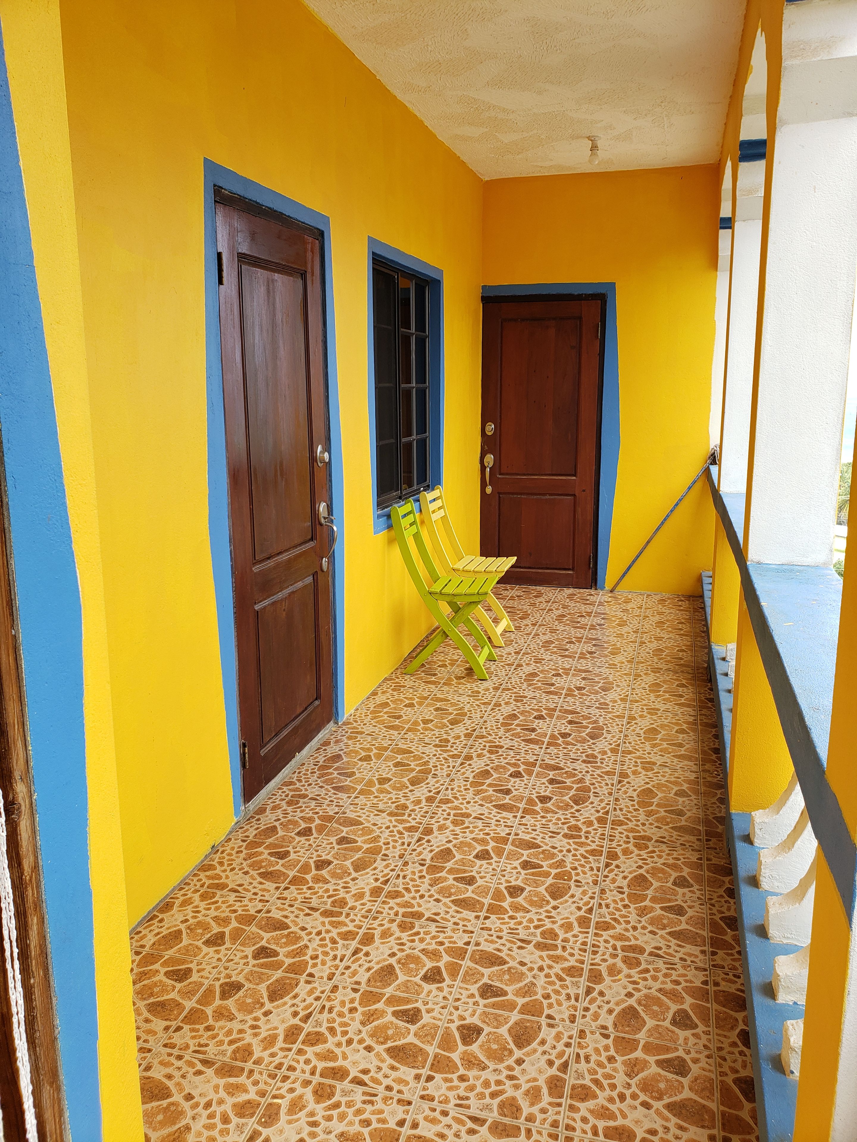 Una escalera con una combinación de colores amarillo y azul, una puerta de madera y una ventana con un contraventanas marrón.