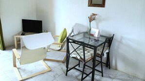Ein gemütlicher Wohnbereich mit Glastisch, zwei Stühlen, einem kleinen Fernseher und einem Kalender an der Wand.