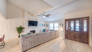 A spacious living room with a large grey sectional sofa, a ceiling fan, a fireplace, and a wooden door with glass panels. - Welcome to your Dream Home, up to 12 guests! (Henderson)