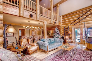Un vaste salon doté d’un haut plafond, de poutres apparentes, d’un magnifique escalier et d’un sapin de Noël décoré.