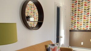 A living room with a sofa, a round mirror, a lamp, and a patterned rug. - The Strand House with hot tub (Kingston)