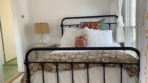 A bedroom with a metal bed frame, white bedding, a fluffy white rug, and a bedside table with a lamp. - The Strand House with hot tub (Kingston)