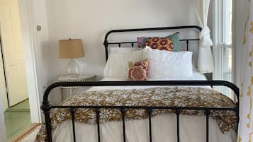A bedroom with a metal bed frame, white bedding, a fluffy white rug, and a bedside table with a lamp.
