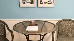 A round glass table with wicker chairs, two framed tropical leaf paintings on the wall, and a small bowl and scissors on the table. - GREAT LAKEVIEW  LOCATION WITH TROPICAL VIBES (Lake Ozark)