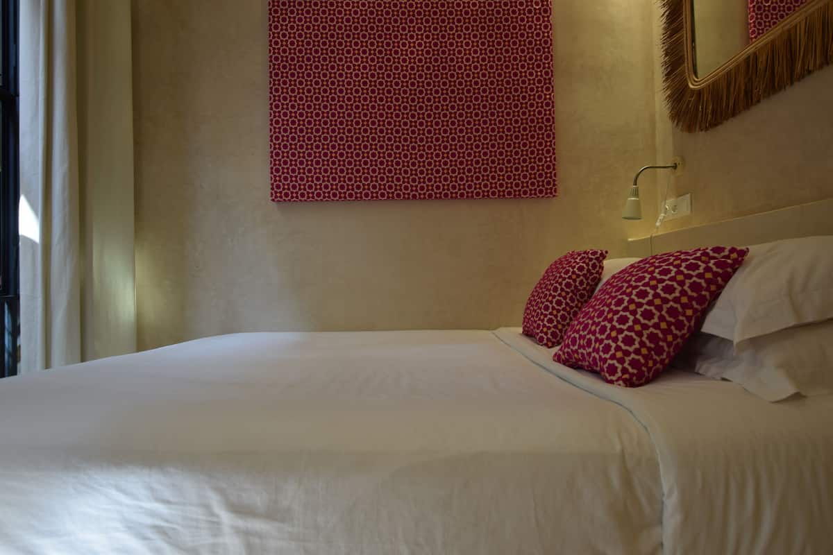 A neatly made bed with white linens and two patterned pillows.