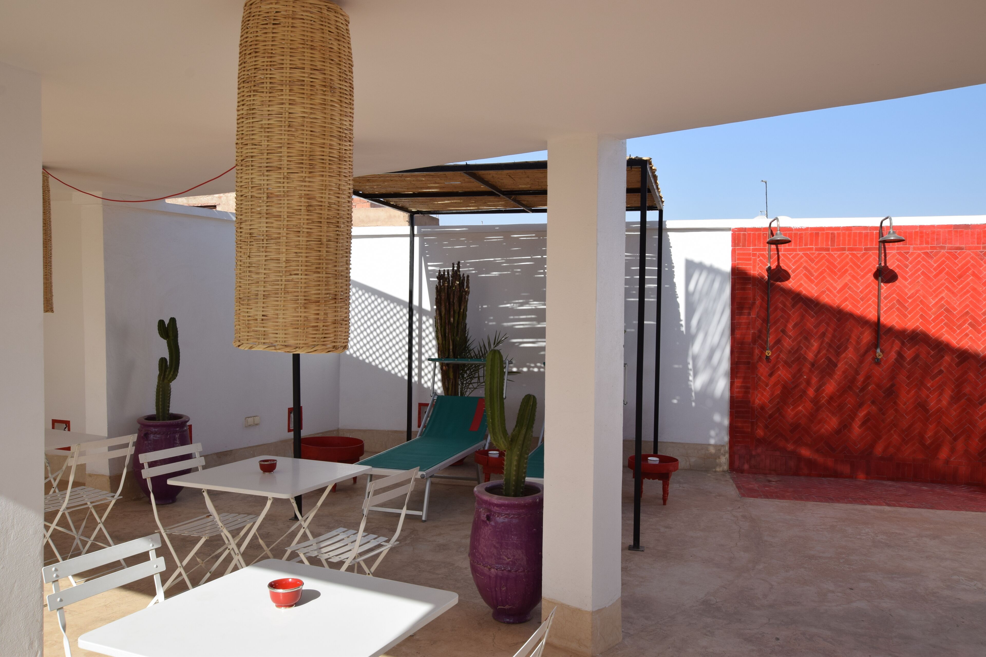 Un patio exterior con una mesa y sillas blancas, un colgante de mimbre y una pared con estampado de escamas de pescado rojas.