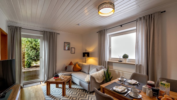 A modern living room with a sofa, coffee table, and dining table set for breakfast. - Ferienapartment Weber (Faßberg)