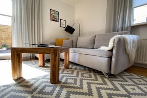 Un salon avec un canapé gris, une table basse en bois, un tapis à motifs et un lampadaire noir.