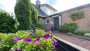 A garden with purple flowers and a brick house with a door and window. - Ferienapartment Weber (Faßberg)