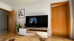 A modern living room with a flat-screen TV on a wooden TV stand, a potted plant, and a wooden coffee table. - Ferienapartment Weber (Faßberg)
