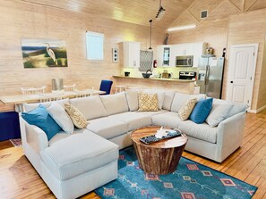 En moderne stue med en stor stribet sofa, et sofabord og et køkken i baggrunden.