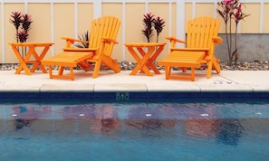 A poolside area with three orange Adirondack chairs and a small table.